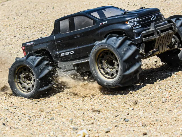 A black monster truck throwing dirt on a gravel track